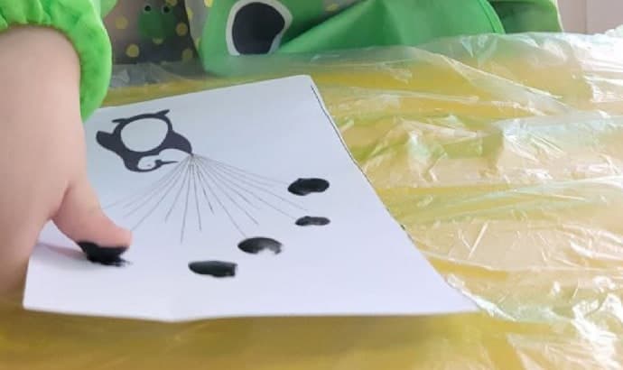A child's hand pressing black fingerprints onto paper during a painting activity at the nursery