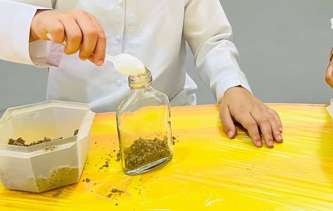 A close view of a child spooning sand into a glass jar during a sensory activity at the nursery