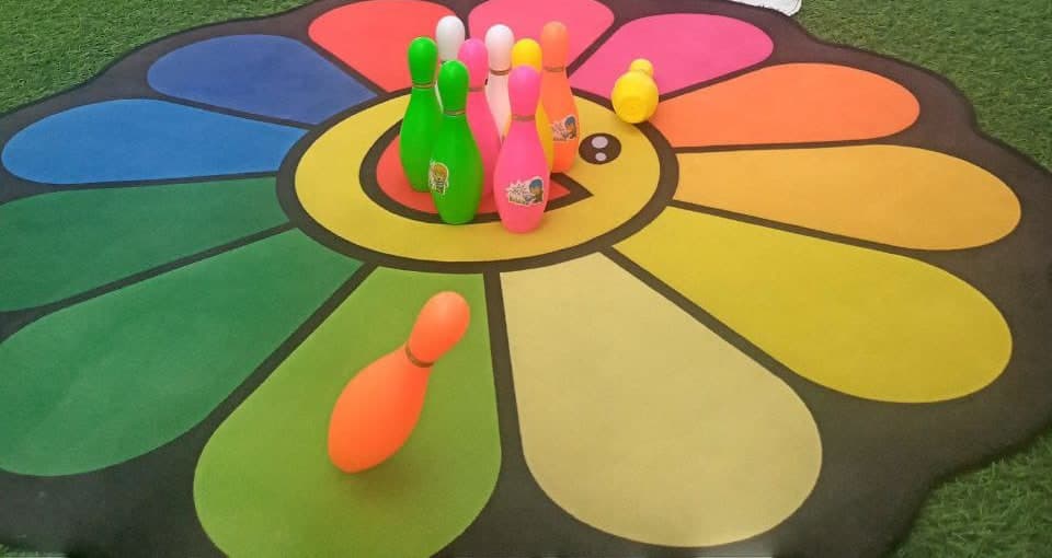 A flower-shaped play mat with coloured skittles on the artificial grass of the outdoor play area at Kids Are Kids Nursery, Ajman